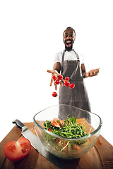 Image showing Amazing african-american man preparing unbelievable food with close up action, details and bright emotions, professional cook. Adding cherry tomatos to salad on the fly