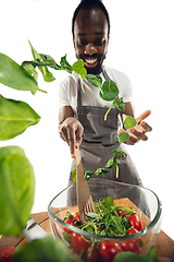 Image showing Amazing african-american man preparing unbelievable food with close up action, details and bright emotions, professional cook. Adding salad greens on the fly