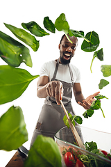 Image showing Amazing african-american man preparing unbelievable food with close up action, details and bright emotions, professional cook. Adding salad greens on the fly