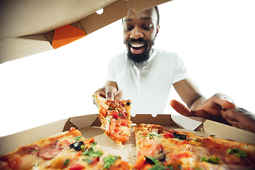 Image showing Amazing african-american man preparing unbelievable food with close up action, details and bright emotions, professional cook. View from out the box with pizza