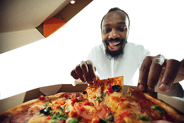 Image showing Amazing african-american man preparing unbelievable food with close up action, details and bright emotions, professional cook. View from out the box with pizza