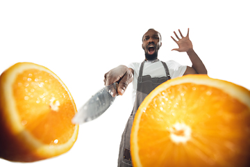 Image showing Amazing african-american man preparing unbelievable food with close up action, details and bright emotions, professional cook. Cutting orange on the fly