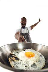 Image showing Amazing african-american man preparing unbelievable food with close up action, details and bright emotions, professional cook. Preparing fried eggs