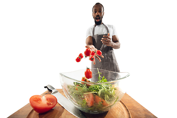 Image showing Amazing african-american man preparing unbelievable food with close up action, details and bright emotions, professional cook. Adding cherry tomatos to salad on the fly