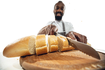 Image showing Amazing african-american man preparing unbelievable food with close up action, details and bright emotions, professional cook. Cutting bread