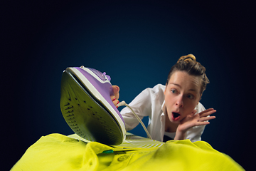 Image showing Close up of young caucasian woman ironing bright clothes with expressive emotions in action, motion