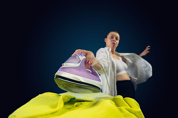Image showing Close up of young caucasian woman ironing bright clothes with expressive emotions in action, motion