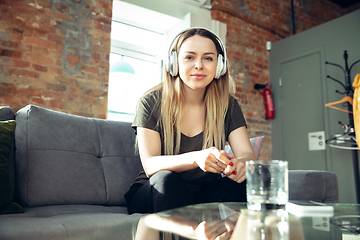 Image showing Young woman wearing wireless headphones gesturing during a video conference in the living room. Attented listening