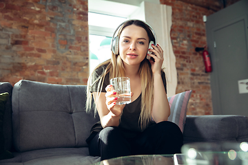 Image showing Young woman wearing wireless headphones gesturing during a video conference in the living room. Attented listening