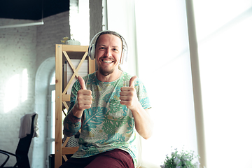 Image showing Young man gesturing during a video conference in the living room. Thummb up, smiling