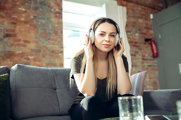 Image showing Young woman wearing wireless headphones gesturing during a video conference in the living room. Attented listening