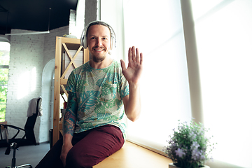 Image showing Young man gesturing during a video conference in the living room. Waving, smiling