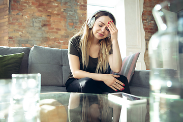 Image showing Young woman wearing wireless headphones gesturing during a video conference in the living room. Upset, headache, tired