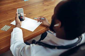 Image showing Doctor advising the patient online with smartphone. African-american doctor during his videocall, work with patients, explaining recipes for drug, checking symptoms