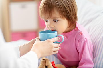 Image showing doctor giving hot tea to sick little girl in bed