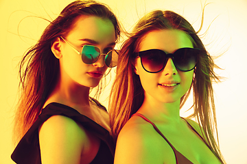 Image showing Close up beautiful girls in fashionable swimsuits and eyewear isolated on yellow studio background in neon light. Summer, resort, fashion and weekend concept.