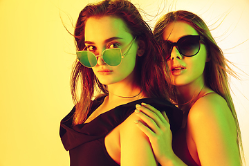 Image showing Close up beautiful girls in fashionable swimsuits and eyewear isolated on yellow studio background in neon light. Summer, resort, fashion and weekend concept.