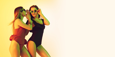 Image showing Beautiful girls in fashionable swimsuits isolated on yellow studio background in neon light. Summer, resort, fashion and weekend concept. Flyer with copyspace.