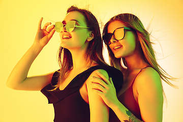 Image showing Close up beautiful girls in fashionable swimsuits and eyewear isolated on yellow studio background in neon light. Summer, resort, fashion and weekend concept.