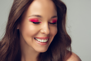 Image showing Close up of beautiful young woman with long healthy curly hair and bright make up isolated on grey studio backgroud, shy smiling