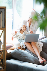 Image showing Mother and daughter, sisters have quite, beauty and fun day together at home. Comfort and togetherness. Watching series using laptop near window wearing white bathrobes