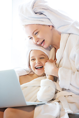 Image showing Mother and daughter, sisters have quite, beauty and fun day together at home. Comfort and togetherness. Watching series using laptop near window wearing white bathrobes