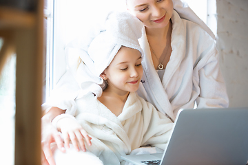 Image showing Mother and daughter, sisters have quite, beauty and fun day together at home. Comfort and togetherness. Watching series using laptop near window wearing white bathrobes