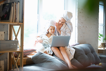 Image showing Mother and daughter, sisters have quite, beauty and fun day together at home. Comfort and togetherness. Watching series using laptop near window wearing white bathrobes