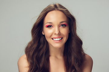 Image showing Close up of beautiful young woman with long healthy curly hair and bright make up isolated on grey studio backgroud, smiling with white teeth