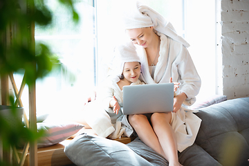 Image showing Mother and daughter, sisters have quite, beauty and fun day together at home. Comfort and togetherness. Watching series using laptop near window wearing white bathrobes