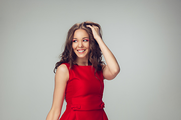 Image showing Beautiful young woman with long healthy curly hair and bright make up wearing red dress isolated on grey studio backgroud. Smiling.