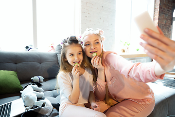 Image showing Mother and daughter, sisters have quite, beauty and fun day together at home. Comfort and togetherness. Do a make up, using cosmetics, masks, moisturizers, brushes and lipsticks, taking selfie