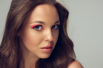 Image showing Close up of beautiful young woman with long healthy curly hair and bright make up isolated on grey studio backgroud, looking serious