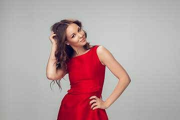 Image showing Beautiful young woman with long healthy curly hair and bright make up wearing red dress isolated on grey studio backgroud. Shiny and confident.