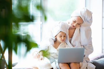Image showing Mother and daughter, sisters have quite, beauty and fun day together at home. Comfort and togetherness. Watching series using laptop near window wearing white bathrobes