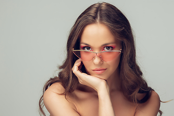 Image showing Close up of beautiful young woman with long healthy curly hair and bright make up wearing stylish pink eyewear isolated on grey studio backgroud