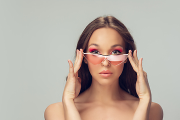 Image showing Close up of beautiful young woman with long healthy curly hair and bright make up wearing stylish pink eyewear isolated on grey studio backgroud