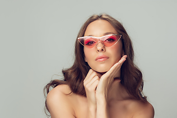 Image showing Close up of beautiful young woman with long healthy curly hair and bright make up wearing stylish pink eyewear isolated on grey studio backgroud