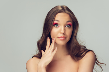 Image showing Close up of beautiful young woman with long healthy curly hair and bright make up isolated on grey studio backgroud, soft touching the cheek