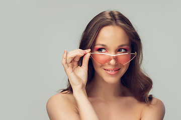 Image showing Close up of beautiful young woman with long healthy curly hair and bright make up wearing stylish pink eyewear isolated on grey studio backgroud, smiling