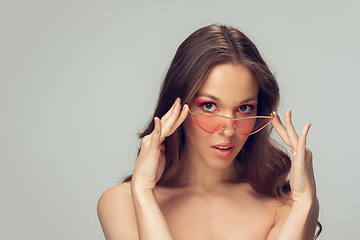 Image showing Close up of beautiful young woman with long healthy curly hair and bright make up wearing stylish pink eyewear isolated on grey studio backgroud