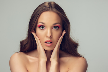 Image showing Close up of beautiful young woman with long healthy curly hair and bright make up isolated on grey studio backgroud, shocked with hands on her face