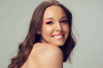 Image showing Close up of beautiful young woman with long healthy curly hair and bright make up isolated on grey studio backgroud, shy smiling