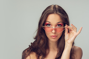 Image showing Close up of beautiful young woman with long healthy curly hair and bright make up wearing stylish pink eyewear isolated on grey studio backgroud