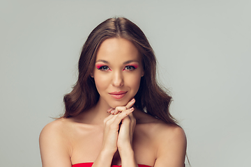 Image showing Close up of beautiful young woman with long healthy curly hair and bright make up isolated on grey studio backgroud, smiling cute