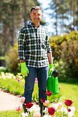 Image showing happy man with watering can and flowers at garden