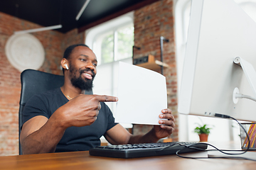 Image showing Young man, businessman working in office, looking on blank black computer screen, monitor, holding blank white sheet, whiteboard. Copyspace.