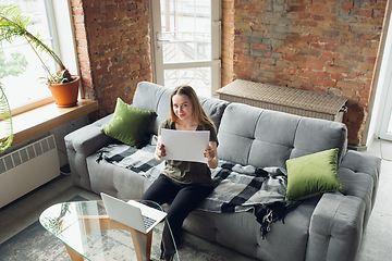 Image showing Young woman, businesswoman working or studying at home, looking on computer screen, monitor, holding white sheet, whiteboard. Attented, concentrated. Copyspace. Top view.