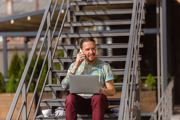 Image showing Young man, businessman working, studying outdoors, looking on computer screen, monitor. Copyspace.