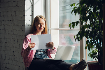 Image showing Young woman, businesswoman working or studying at home holding white sheet, whiteboard. Attented, concentrated. Copyspace. Top view.